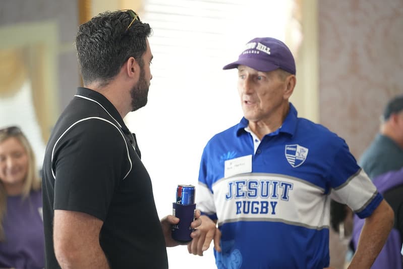An alumnus in a Jesuit Rugby jersey sharing stories at the reunion